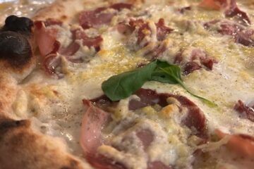 Close-up of authentic Italian pizza, showing bubbly cheese, bright a sprig of fresh basil and finely cured ham